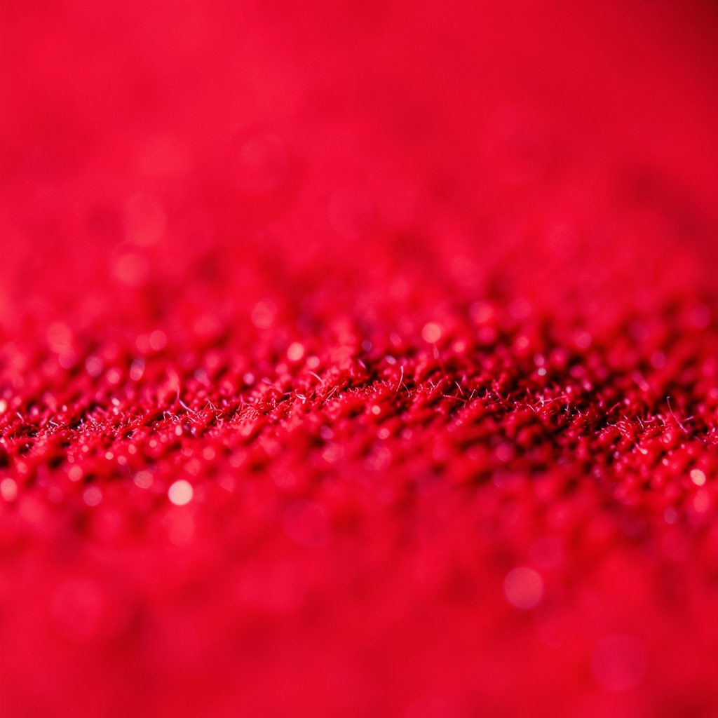 Close-up of matte slate gray fabric texture with a faint red-pink thread running through it, calm and understated