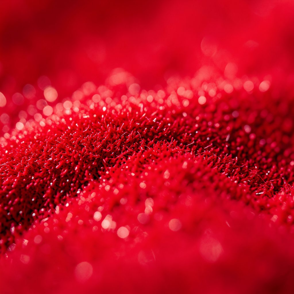 Extreme close-up of a dark textured metallic surface with soft red-pink highlights, moody and industrial